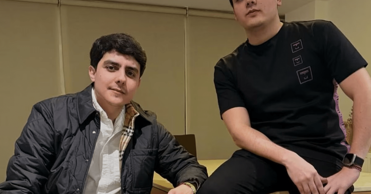 Dos personas en un entorno interior, una sentada con abrigo oscuro y otra de pie con camiseta negra, posiblemente relacionadas con el incidente en Plaza Andares.