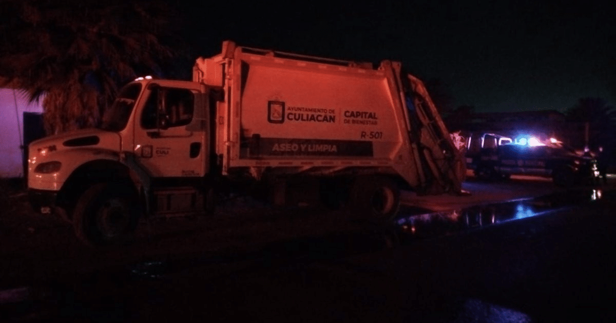 Camión de basura del Ayuntamiento de Culiacán estacionado de noche con luces de emergencia en el fondo.