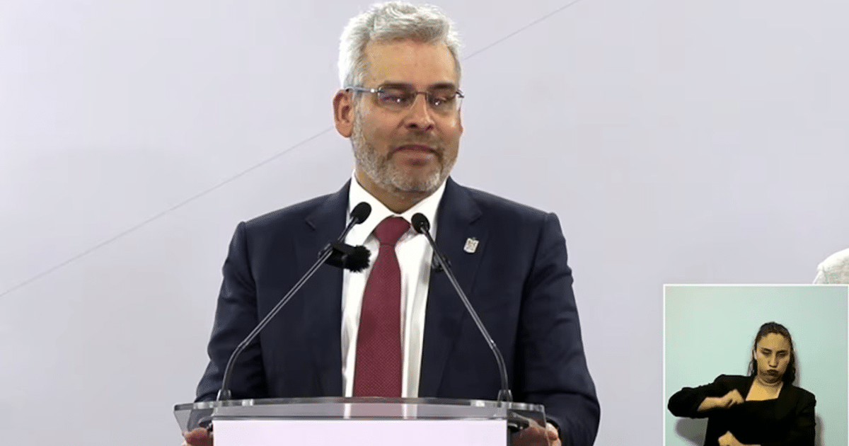 Hombre en traje hablando en un podio con intérprete de lenguaje de señas a su lado en una conferencia.