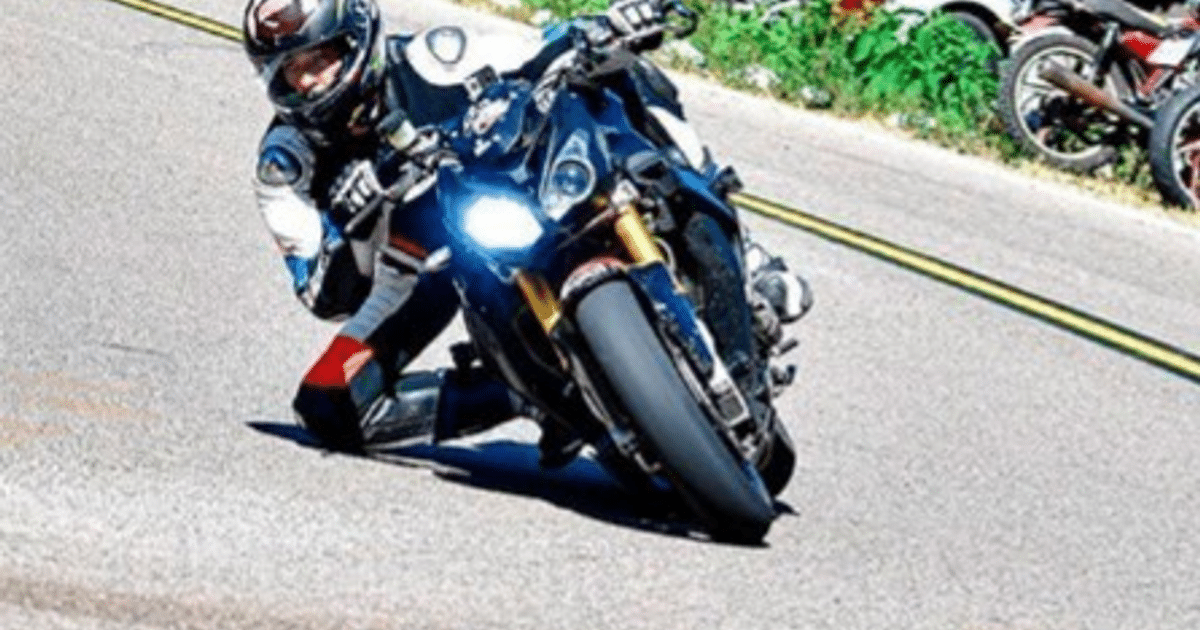 Motociclista inclinado en curva durante el Cain Road Race, con traje de protección y motocicleta de alta gama.