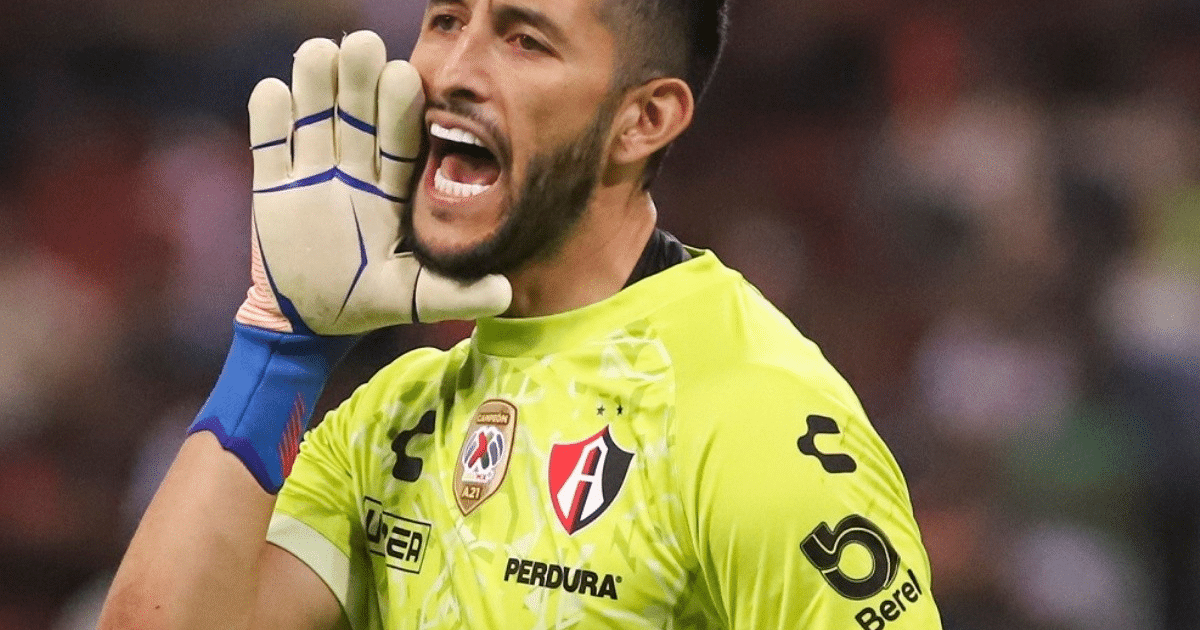 Portero de fútbol gritando instrucciones en el campo, con camiseta verde neón y guantes, en un estadio.