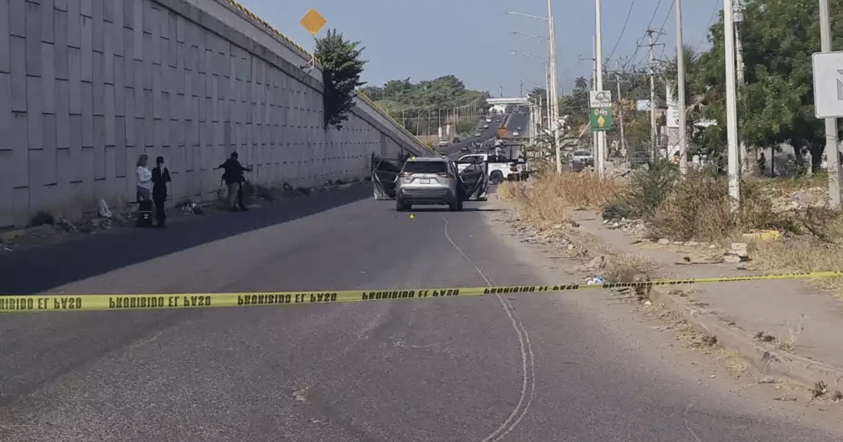 Vehículo baleado en carretera con cinta policial y personas en la acera en Culiacán.