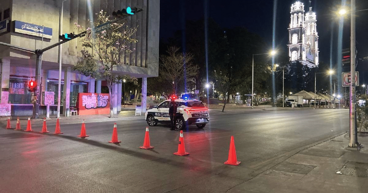 Calle nocturna en Culiacán con vehículo de policía y conos de tráfico durante cierre vial.