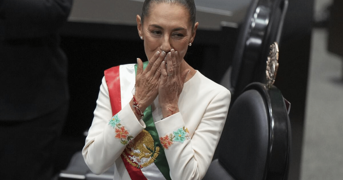 Claudia Sheinbaum en un evento institucional con vestido blanco y banda tricolor, destacando su reconocimiento internacional.