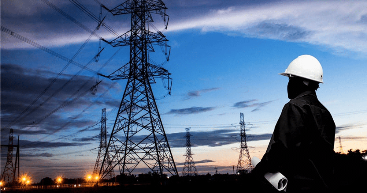 Persona con casco blanco mirando torres eléctricas al atardecer