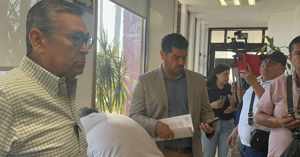 Personas en un entorno laboral en el Palacio Municipal de Ahome, con un hombre en camisa a cuadros y otro en traje claro.