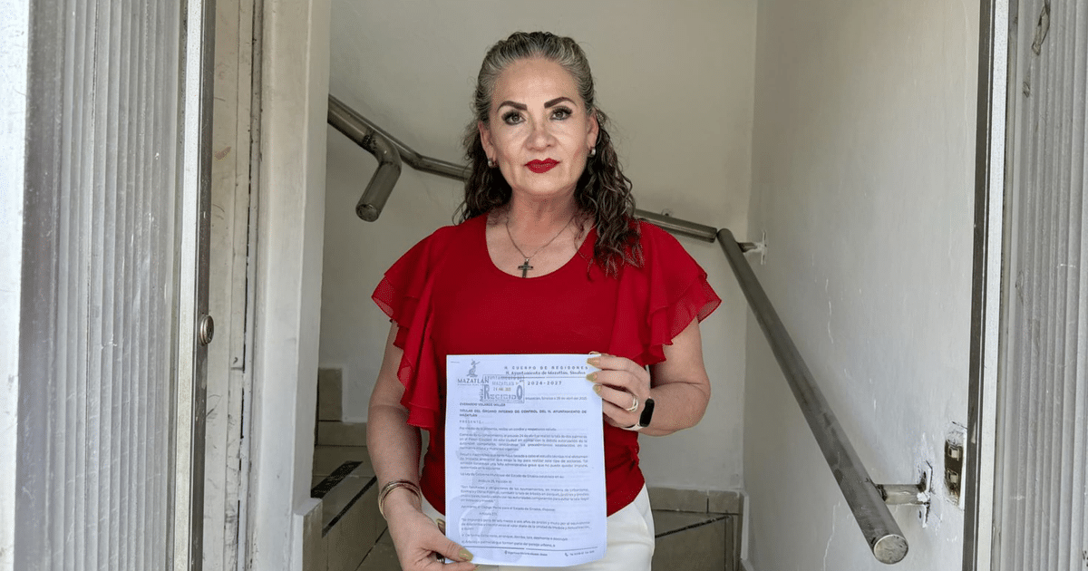 Mujer con blusa roja sosteniendo documento en pasillo de oficina