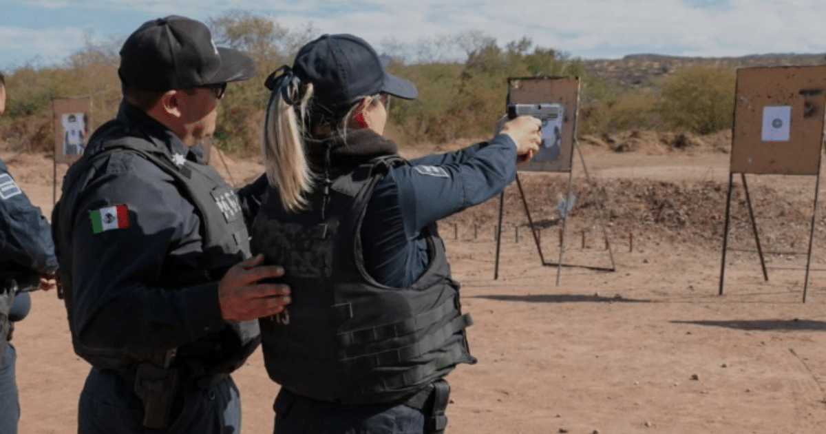 Mujer en chaleco táctico disparando en un campo de tiro desértico, observada por un asistente.