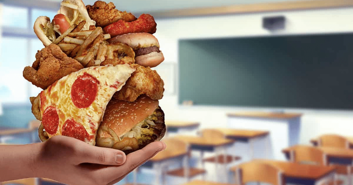 Mano sosteniendo comida rápida en un aula, simbolizando la regulación de alimentos en escuelas.