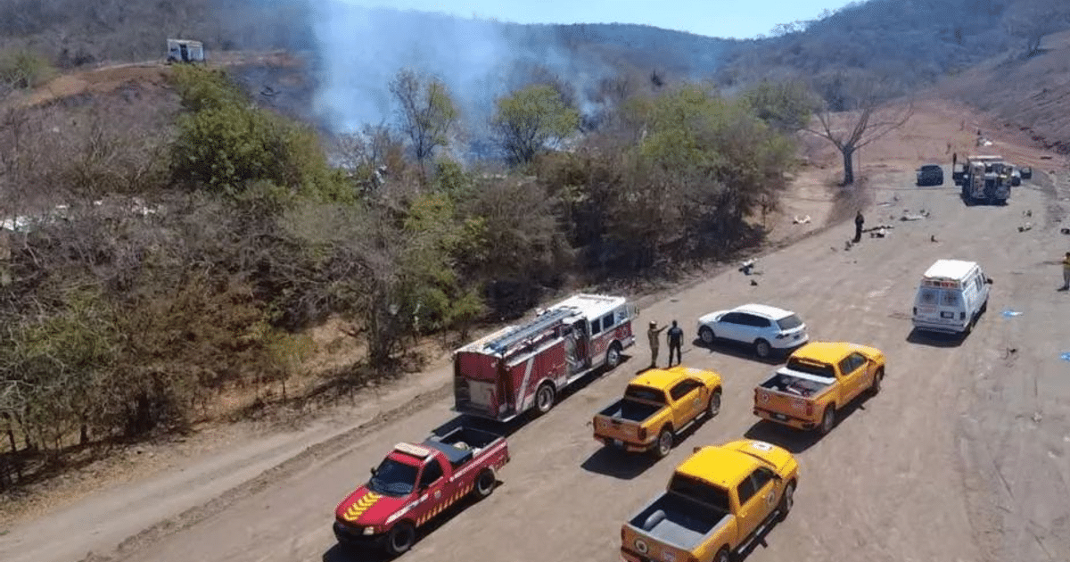 Camiones de bomberos y ambulancias en una carretera rural con humo en el fondo, tras explosión en El Chilillo.