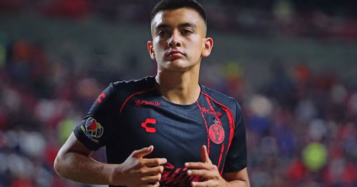 Jugador de fútbol en estadio con camiseta negra y detalles rojos, vinculado a la estrategia de reclutamiento del Ajax.