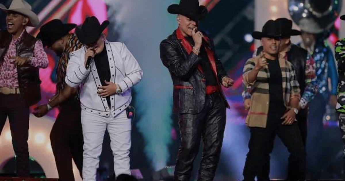Hombres en el escenario con trajes típicos de música regional durante un evento en vivo.