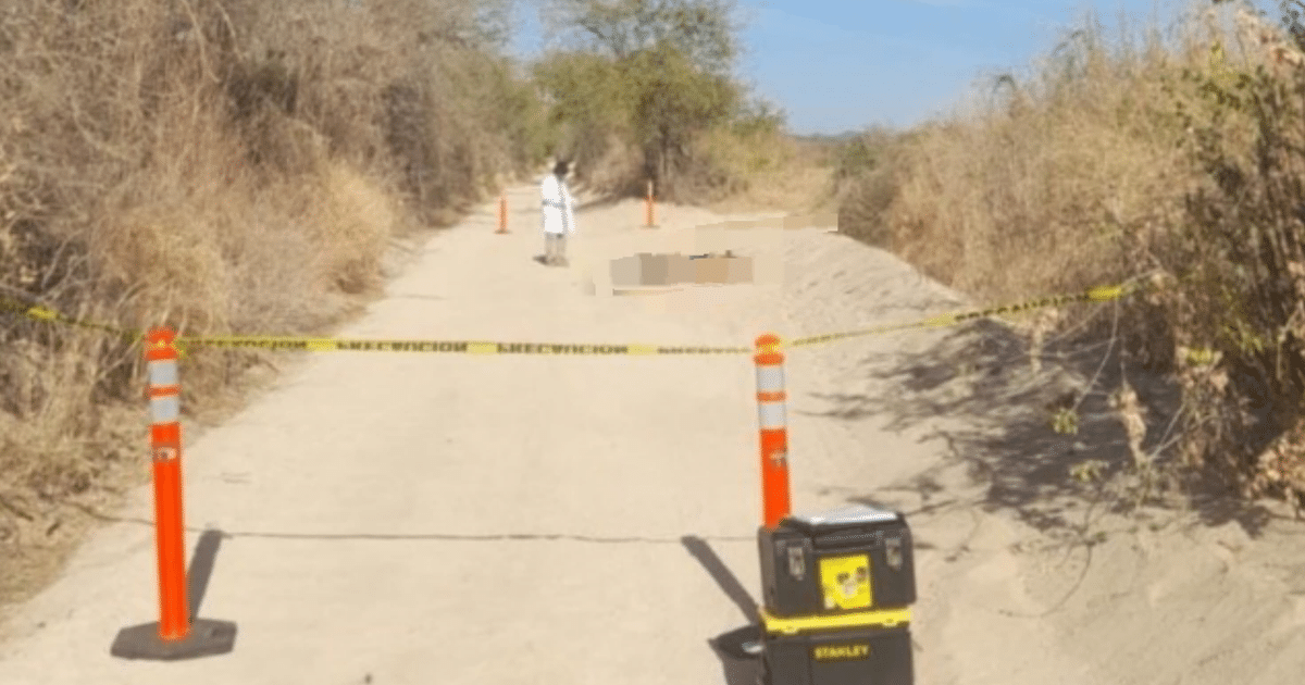 Camino de terracería en Mocorito acordonado por investigación policial, con conos naranjas y una persona en bata blanca al fondo.