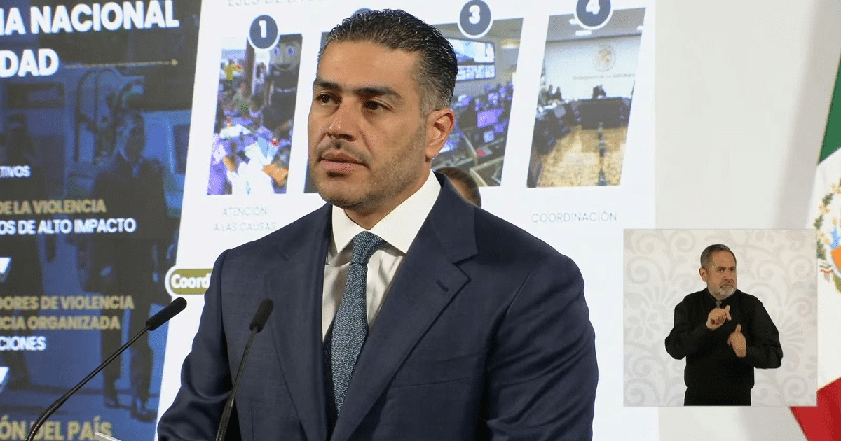 Hombre en conferencia de prensa sobre incidente en Culiacán con intérprete de lengua de señas y bandera de México.