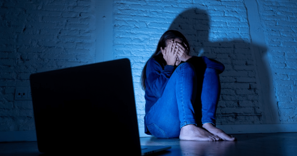 Persona joven sentada en el suelo con un ordenador portátil, iluminada por luz azul, simbolizando angustia y soledad.