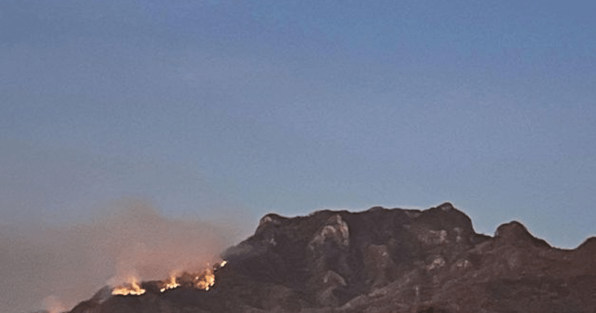 Montaña en El Rosario con humo y llamas, indicando un incendio forestal al amanecer.