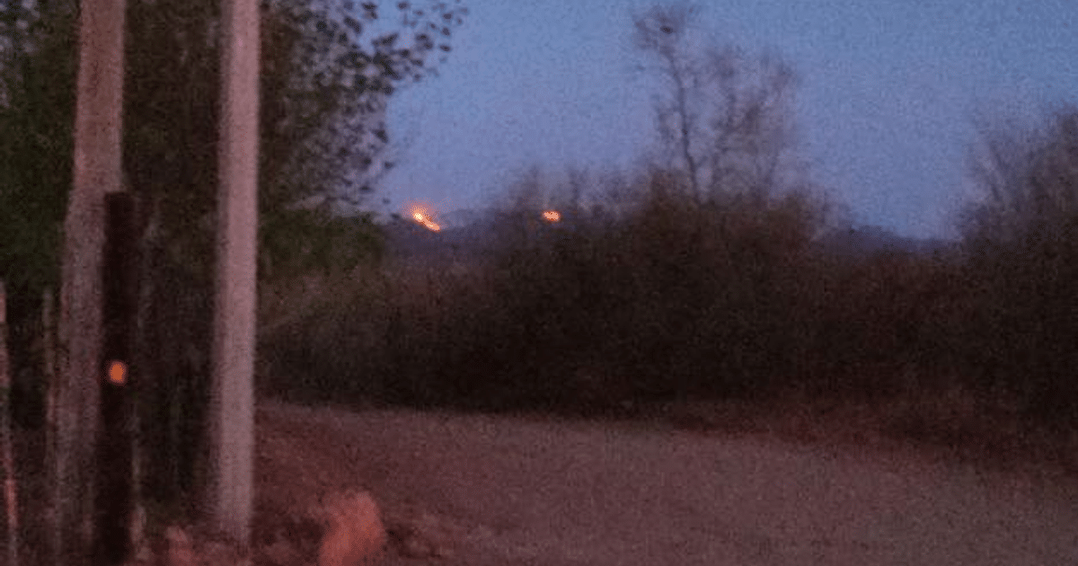 Paisaje crepuscular con carretera de tierra y luces en colina, posiblemente llamas de incendio forestal en El Fuerte.