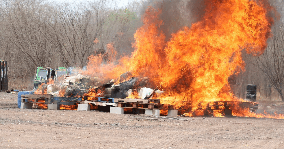 Fuego intenso en incineración de drogas en Sinaloa, con palets de madera y un paisaje desolado de fondo.