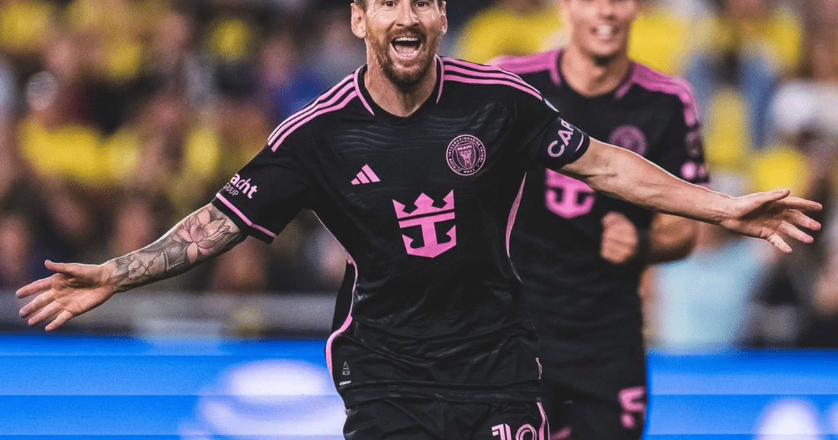 Jugador de fútbol celebrando un gol con los brazos en alto en un estadio lleno de espectadores.