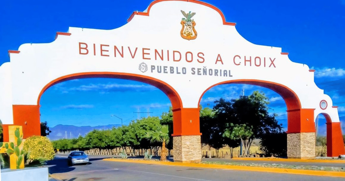 Arco de bienvenida a Choix, Sinaloa, con colores rojo y blanco, cielo azul y plantas alrededor.