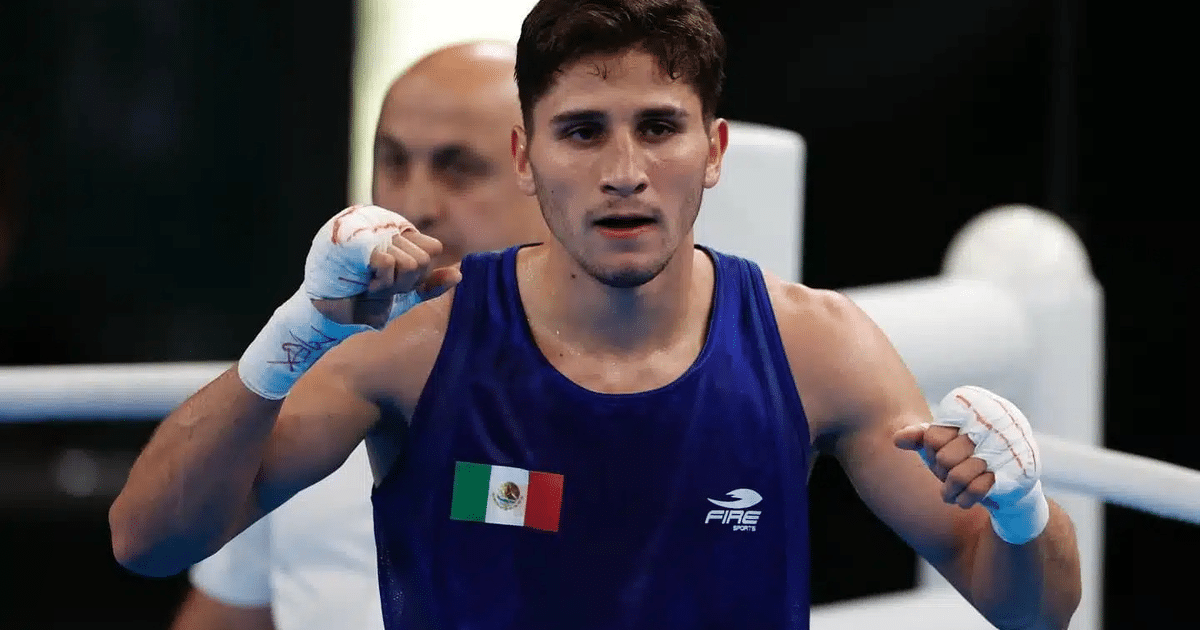 Boxeador mexicano en el ring con camiseta azul y bandera de México, celebrando con manos vendadas.