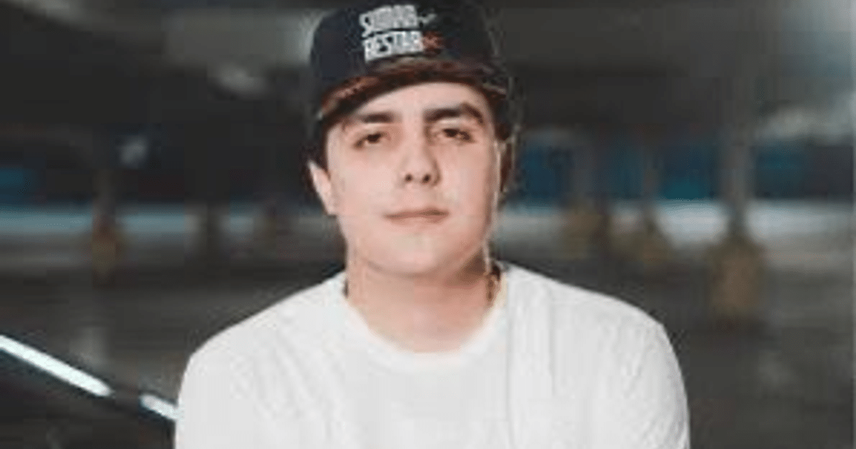 Joven con camiseta blanca y gorra en estacionamiento, vinculado a grabación con Cártel de Sinaloa.