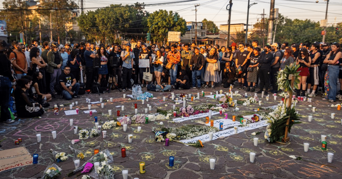 Personas reunidas en una vigilia conmemorativa, con un altar decorado con flores y velas en el centro.