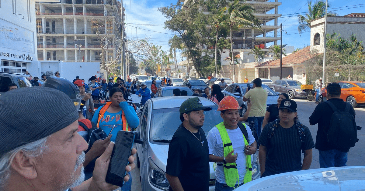 Multitud en Mazatlán protestando por incidente laboral, con personas sosteniendo carteles y un edificio en construcción al fondo.