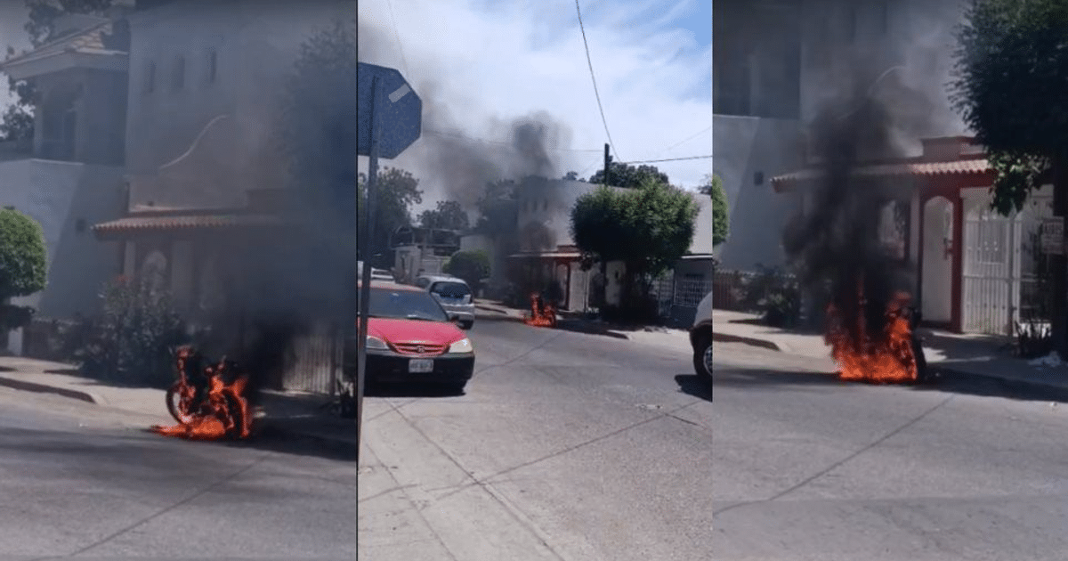 Motocicleta en llamas en la calle con humo negro, vehículos y casa de fondo