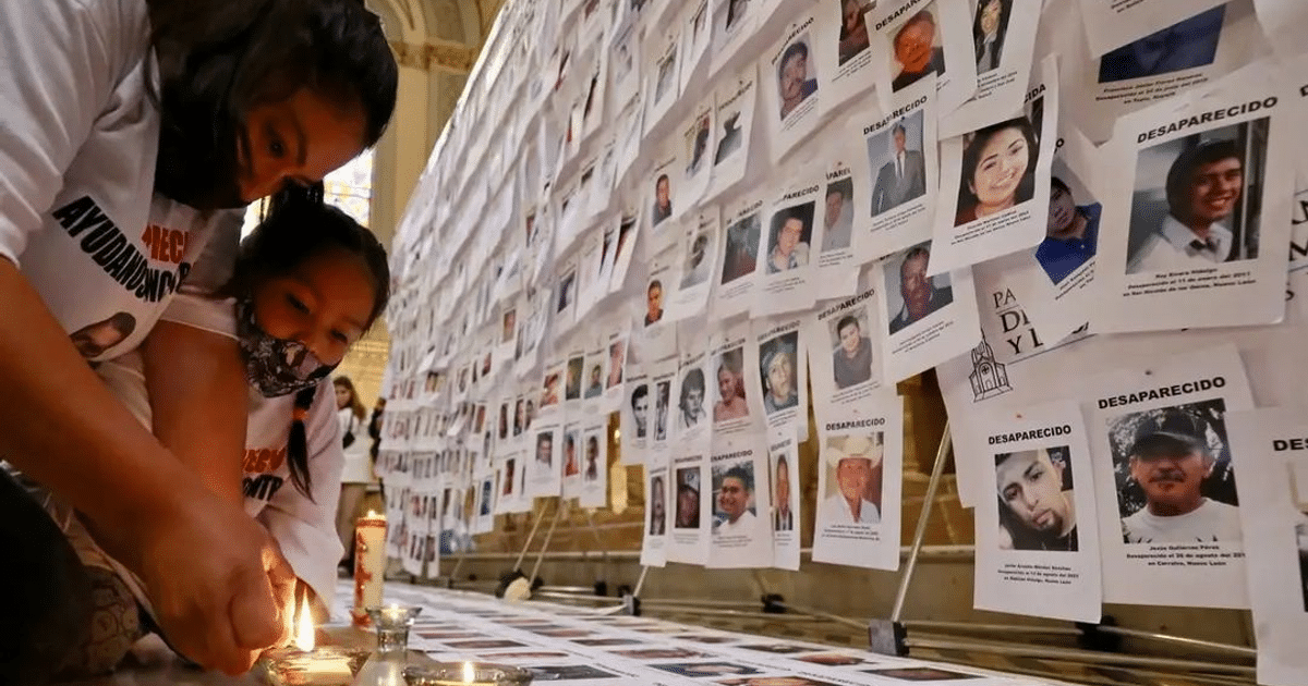 Mujer y niña encendiendo una vela frente a fotos de desaparecidos en México