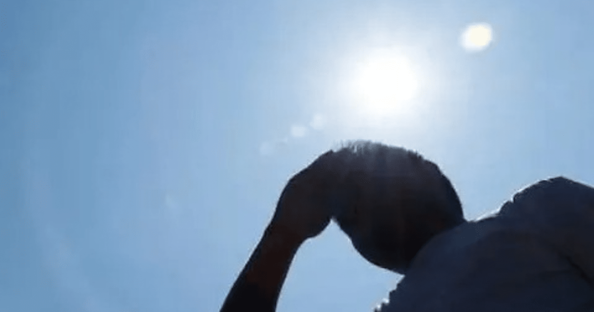 Persona cubriéndose del sol bajo un cielo azul, representando la ola de calor en Sinaloa.