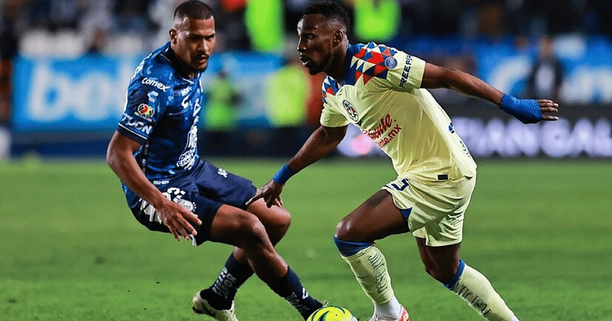 Dos jugadores de fútbol en acción durante un partido, uno con camiseta azul y otro con camiseta amarilla, en un estadio iluminado.