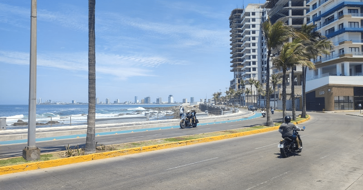 Motociclistas en el paseo marítimo Claussen con palmeras y edificios al fondo.