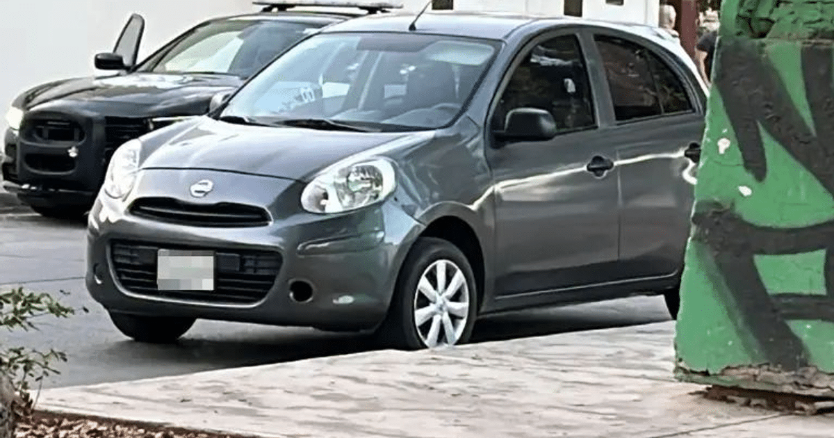 Nissan March gris con impactos de bala en calle de Culiacán, fondo con grafitti verde y negro.