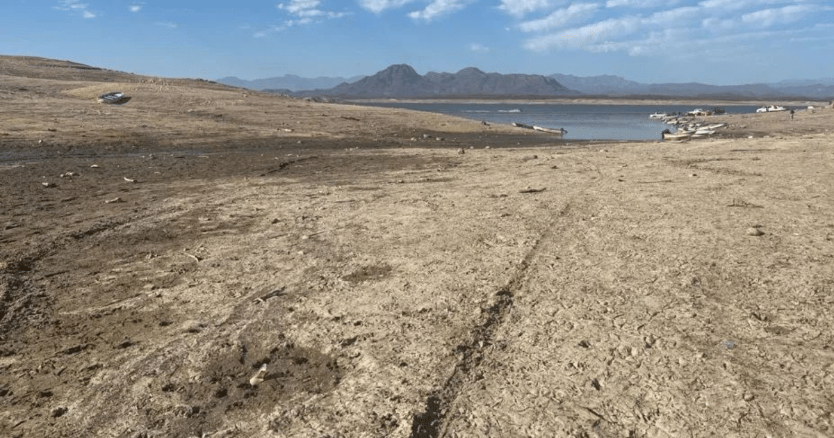 Paisaje árido con montañas, cuerpo de agua y embarcaciones, reflejando sequía.