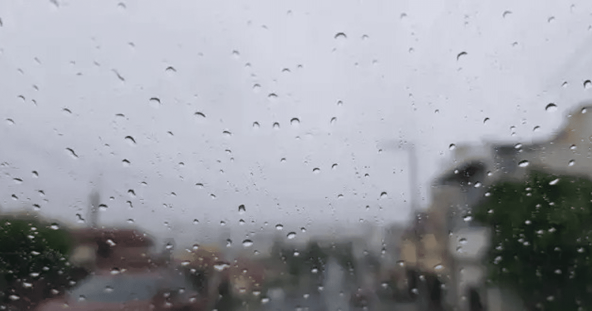Gotas de lluvia en un cristal con edificios y cielo nublado de fondo