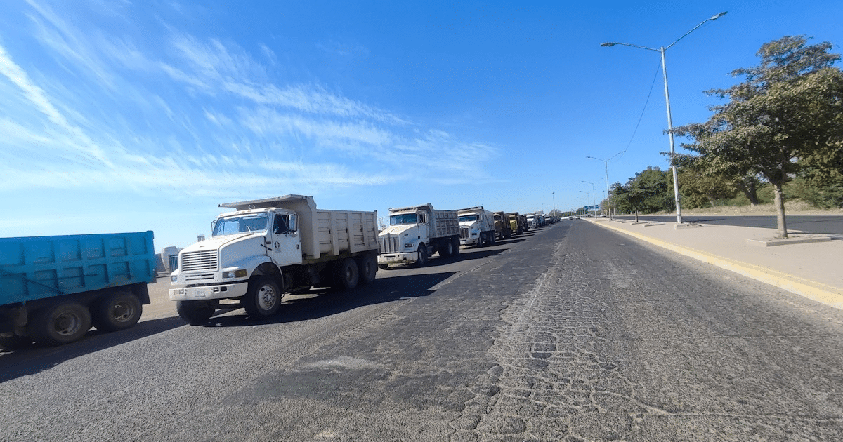 Camiones de carga alineados en protesta en carretera Los Mochis–El Fuerte bajo un cielo azul.