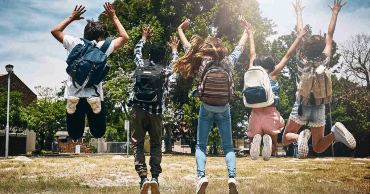 Adolescentes saltando con mochilas en un entorno natural, celebrando el inicio de las vacaciones escolares en Sinaloa.