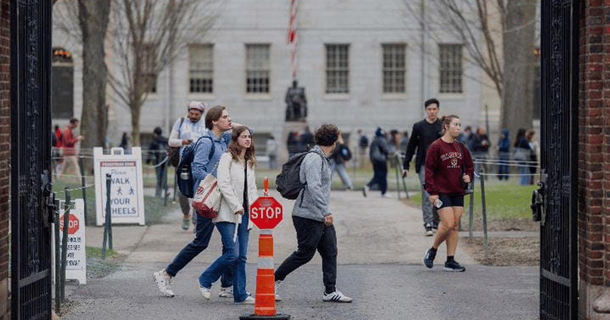 Estudiantes caminando en un campus universitario con señal de STOP y cartel 'WALK ON YOUR HEELS'.