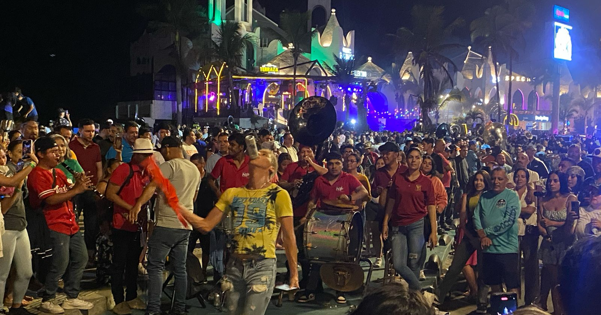 Grupo de personas disfrutando de música en vivo durante la Semana Santa 2025 en Mazatlán, con músicos tocando tambor y tuba bajo luces coloridas.