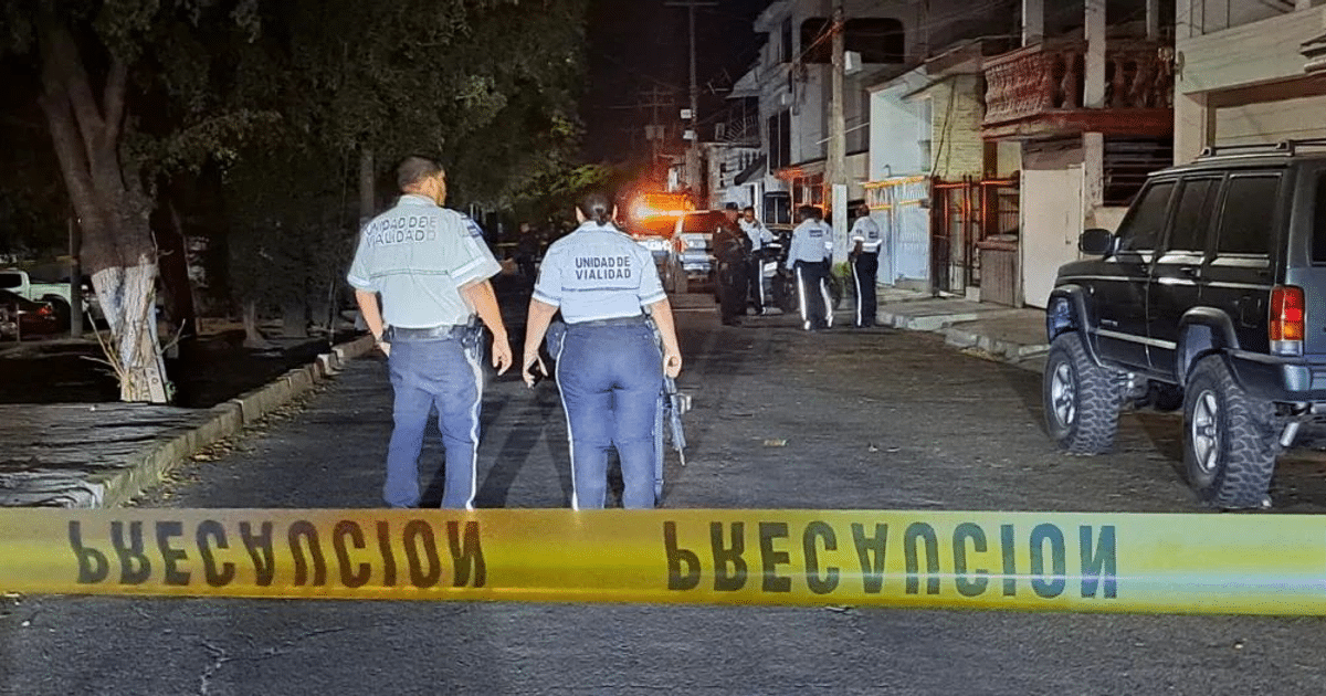 Agentes de policía en una calle de Culiacán con cinta de seguridad amarilla y vehículos oficiales durante la noche.