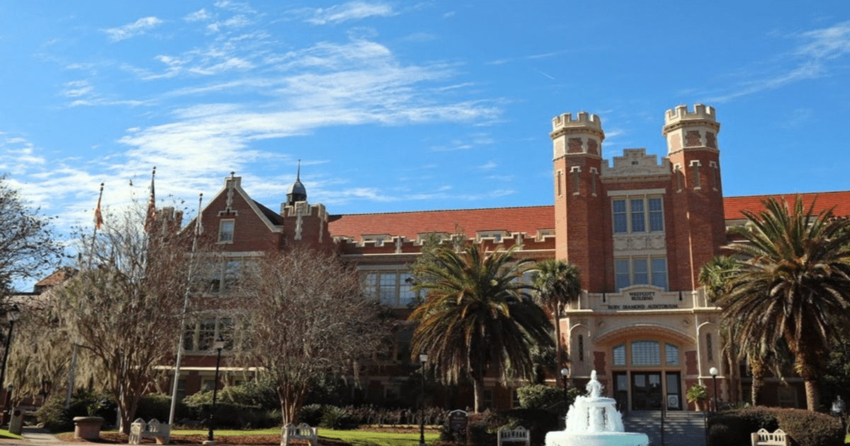 Edificio de ladrillo con torres y palmeras en el campus FSU, cielo azul y banderas ondeando.