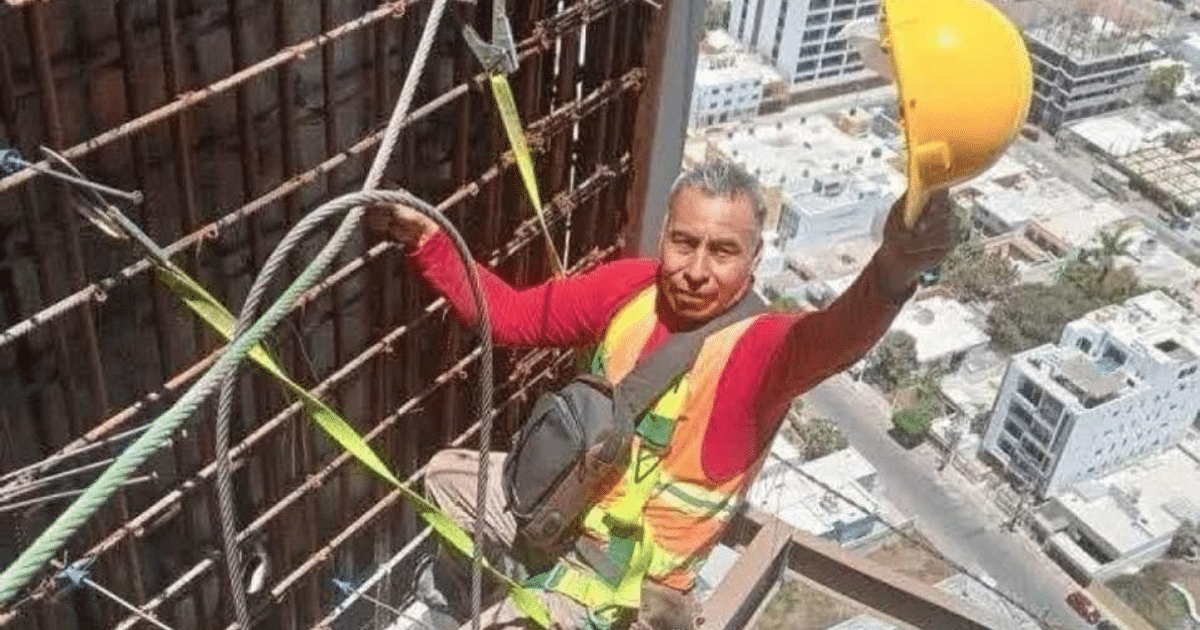 Trabajador de la construcción en estructura alta con casco amarillo y cables, ciudad de fondo.