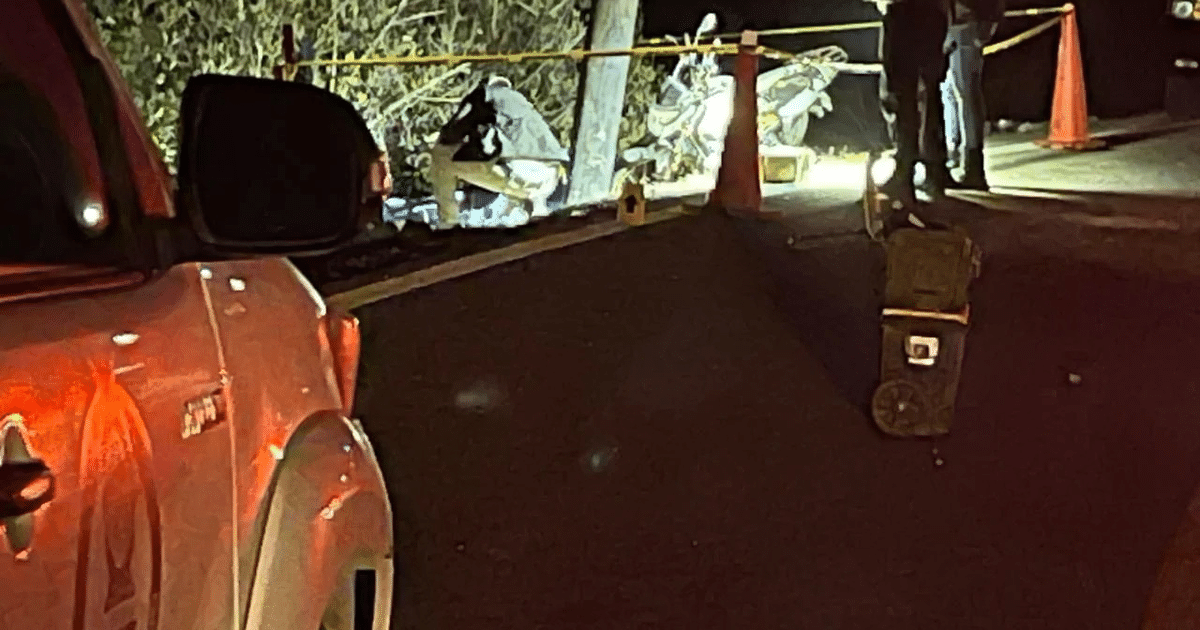 Escena nocturna en carretera con vehículo aparcado, barreras de tráfico y equipo de emergencia trabajando bajo luces brillantes.