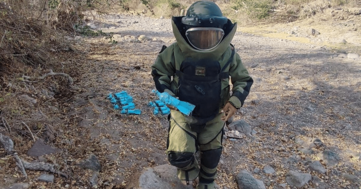 Especialista en desactivación de explosivos en Culiacán con traje de protección, evaluando objetos en un área rocosa.