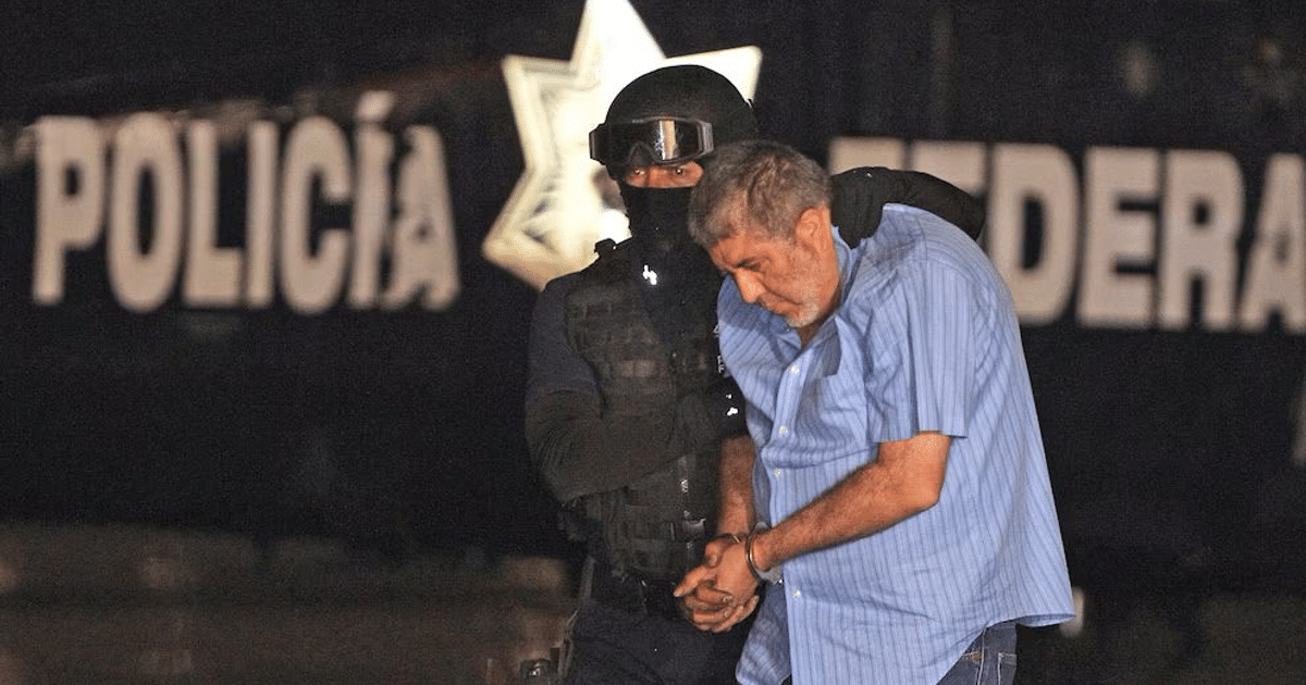 Hombre esposado junto a policía en operativo, vehículo policial al fondo