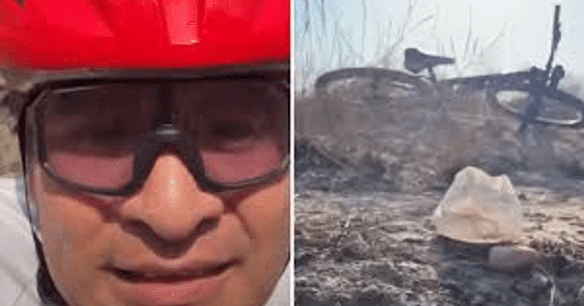 Ciclista con casco rojo y gafas en un entorno seco, junto a una bicicleta y una bolsa en el suelo, en medio de un tiroteo en Culiacán.