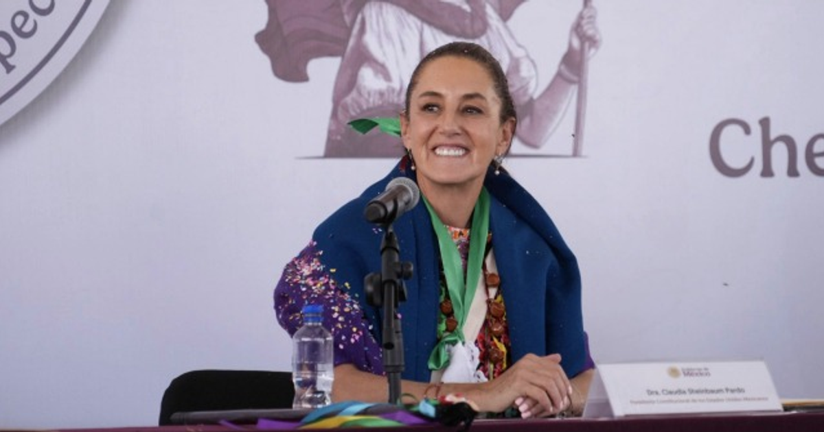 Claudia Sheinbaum en conferencia, vestida con atuendo tradicional, frente a un micrófono.