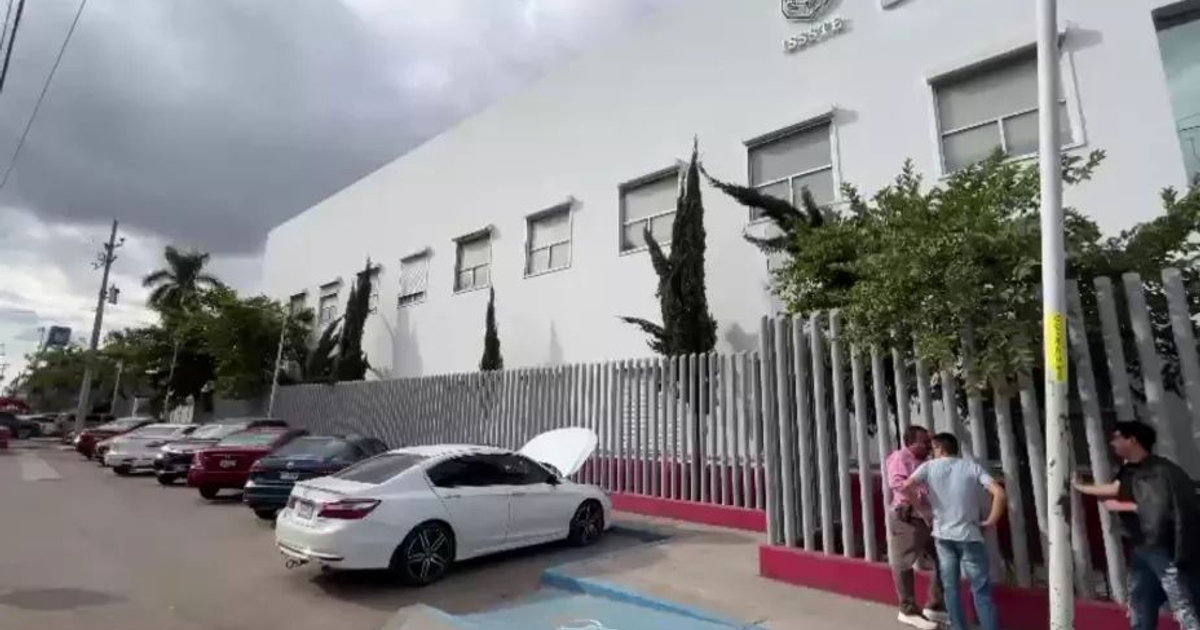 Calle con vehículos estacionados y un automóvil blanco con el capó abierto, relacionada con el ataque a un agente en Culiacán.