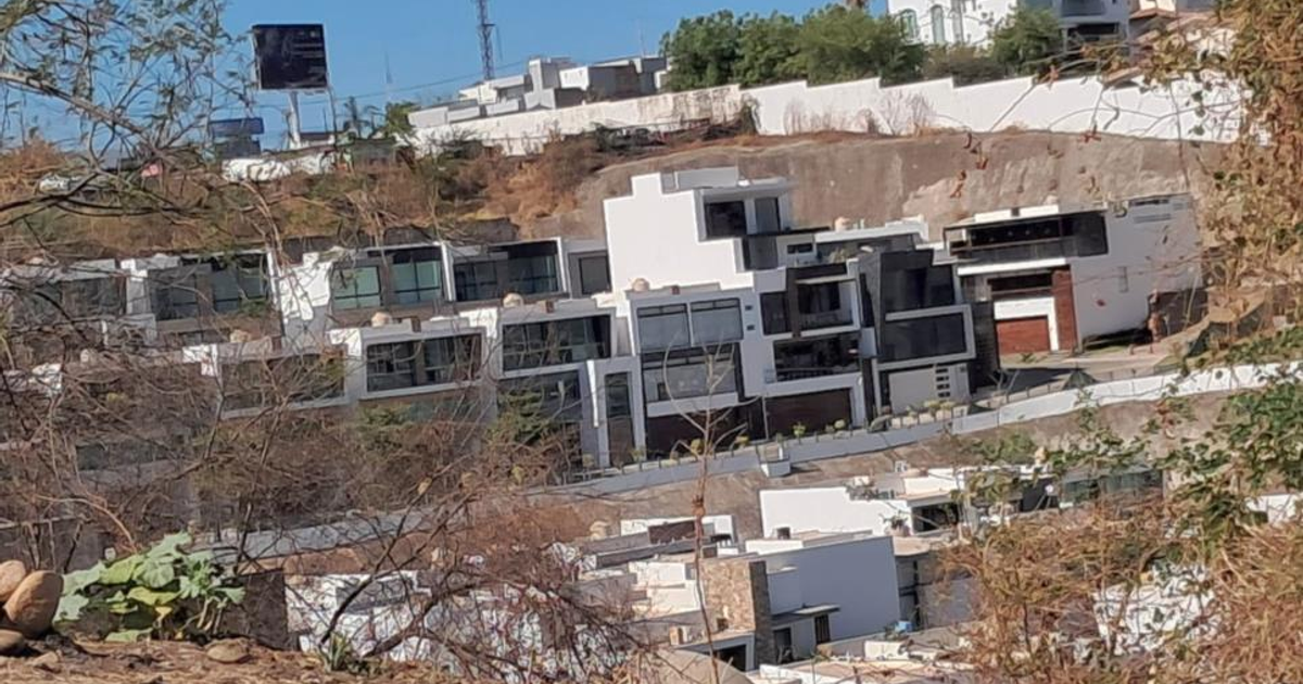 Casas modernas en Colinas de San Miguel, Culiacán, con árboles secos y un letrero al fondo.